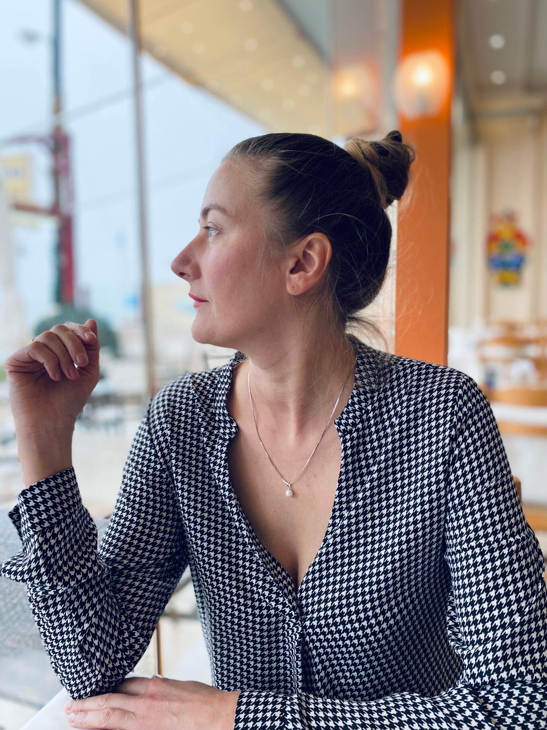 Femme contemplative en veste à motif houndstooth regardant à l'extérieur d'un café